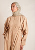 This Maxi Shirt Dress Sand features cuffed sleeves and pockets, giving the appearance of a tucked-in shirt and skirt when it is actually a one-piece outfit. Pleats at the waist create a cinch, while the top half remains loose for a comfortable fit. The dress is cut in an A-line style. Neutral beige tone.